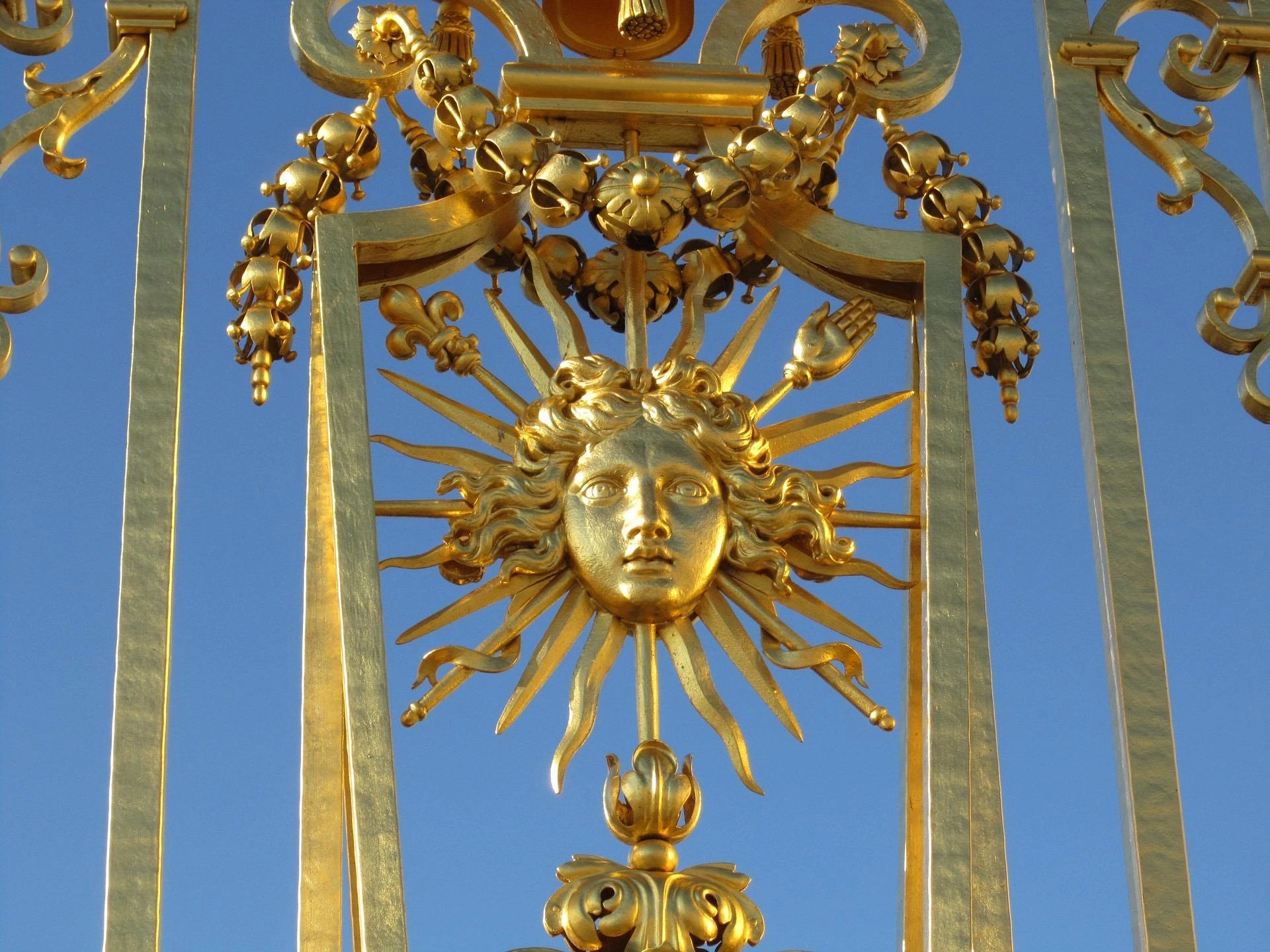 Détail doré de la Grille Royale du Château de Versailles représentant le soleil d'Apollon.